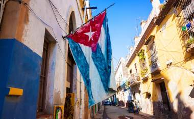Street sidelined by decaying buildings in Old Havana with a big cuban flag