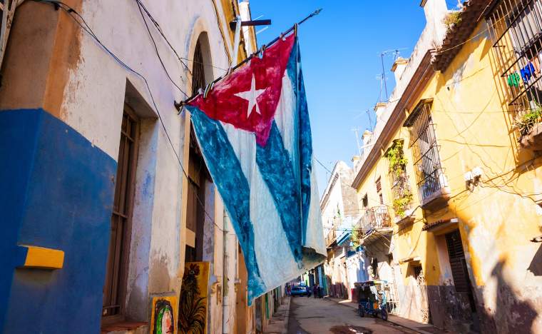 Street sidelined by decaying buildings in Old Havana with a big cuban flag